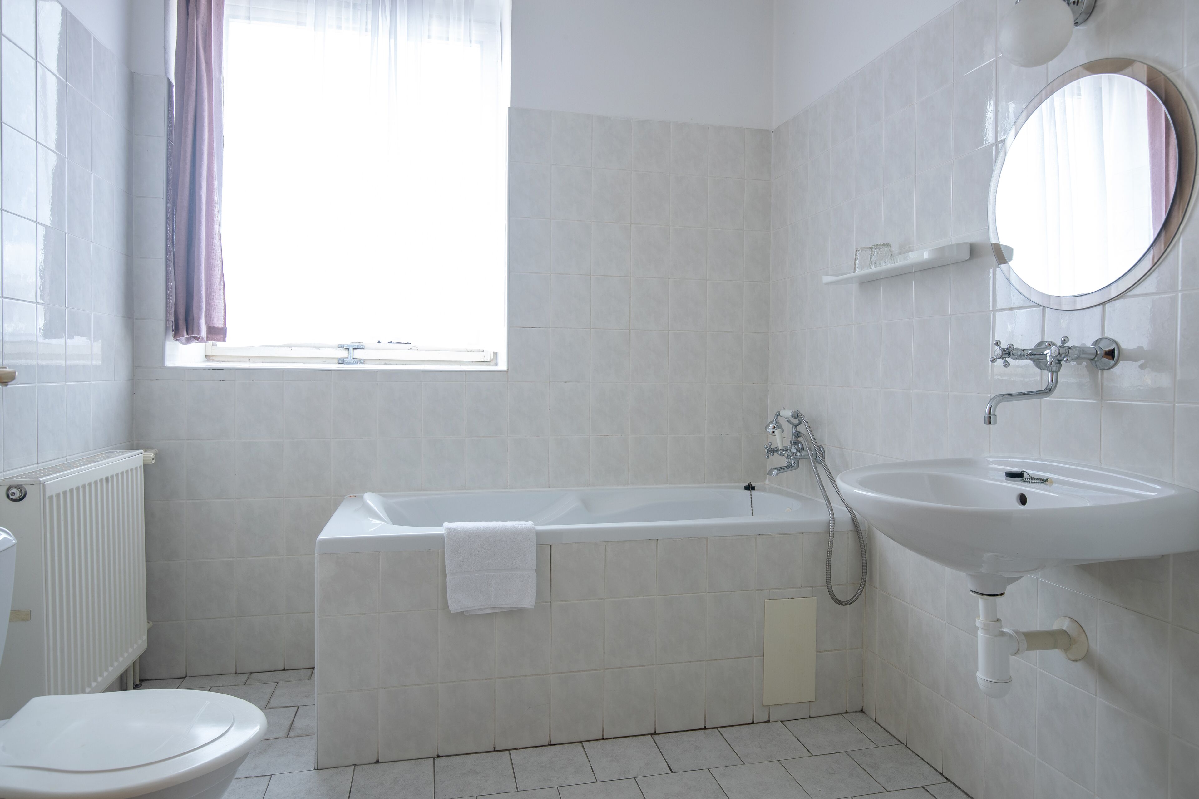 Un baño con bañera, inodoro, lavamanos y ventana con cortinas.