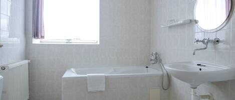 Un baño con bañera, inodoro, lavamanos y ventana con cortinas.