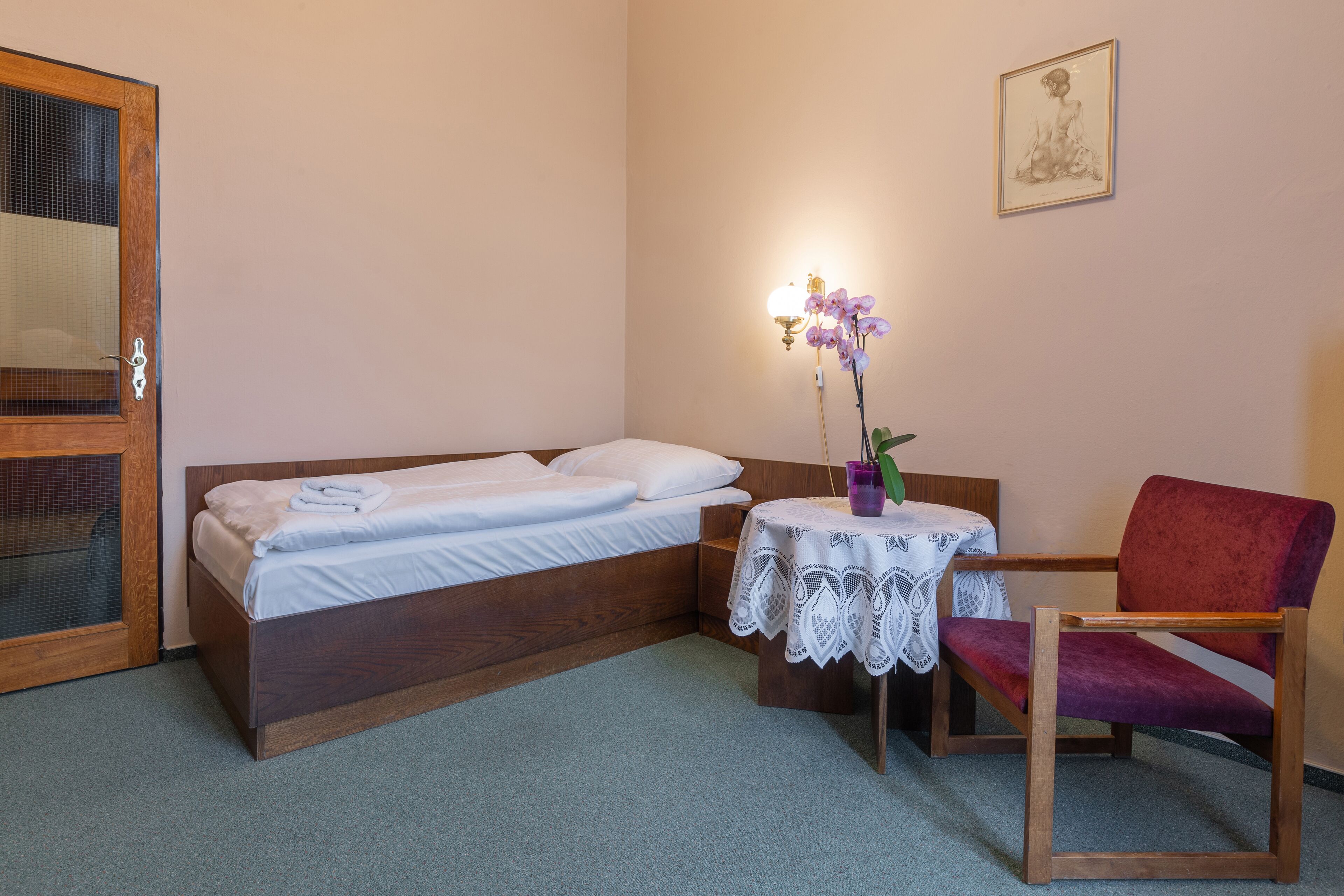 A bedroom with a bed, a chair, a table with a lamp, and a wall-mounted picture.