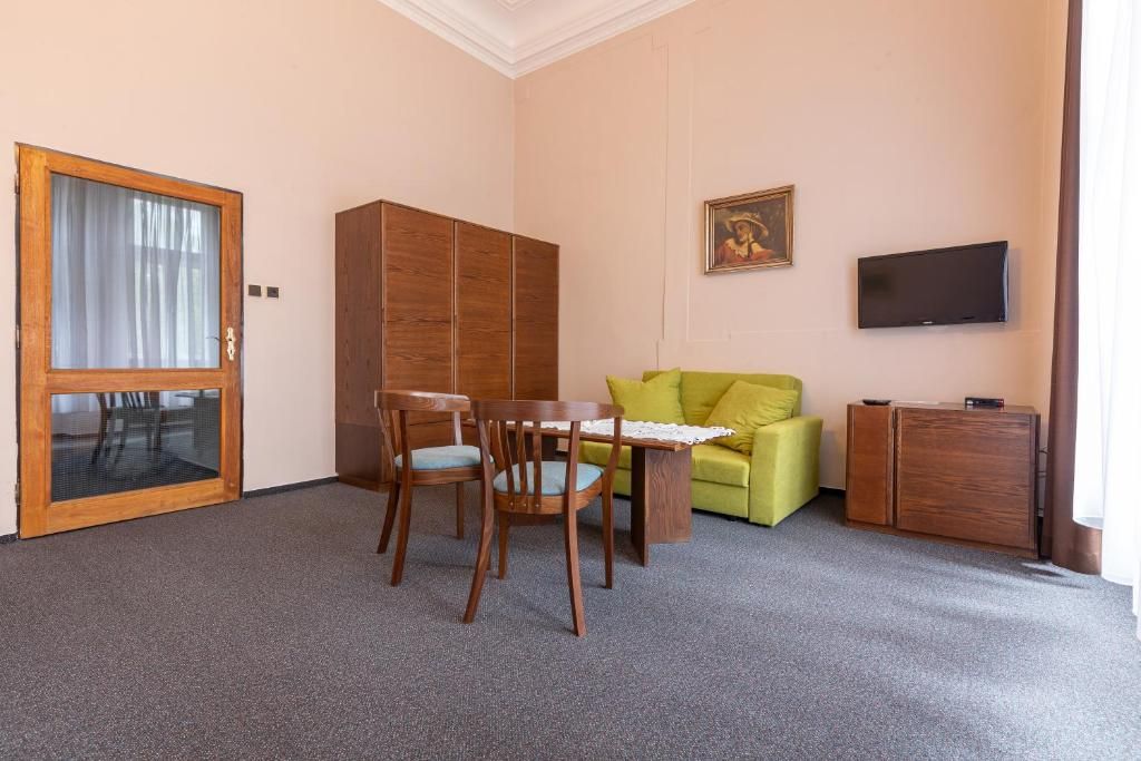 A room with a wooden dining table, two chairs, a green sofa, a television, and a wooden cabinet.