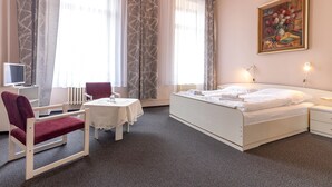 Ein Hotelzimmer mit Bett, Schreibtisch, Stuhl, Tisch und einem Gemälde an der Wand.