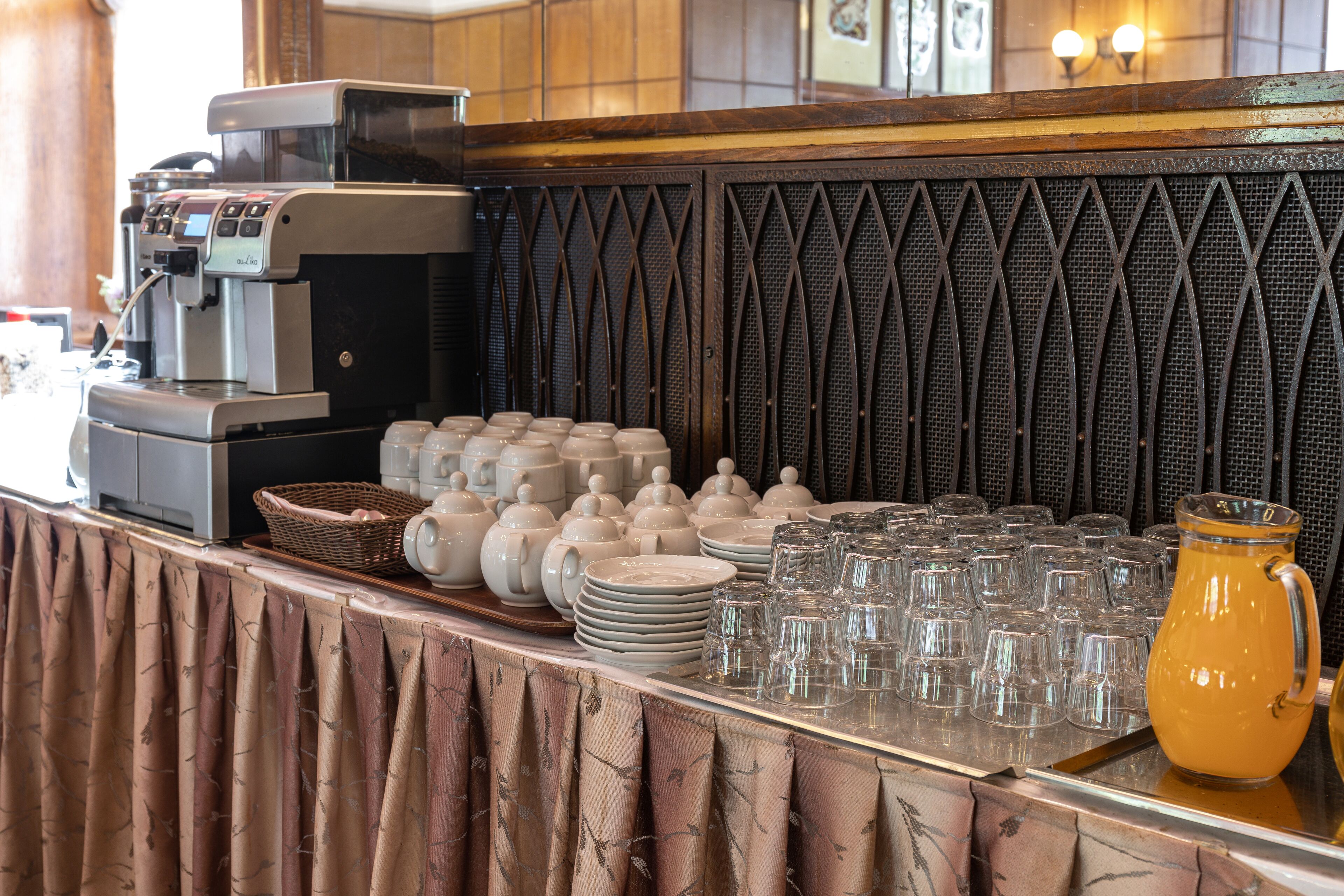 Una mesa de buffet con una máquina de café, sets de té y una jarra de jugo de naranja.