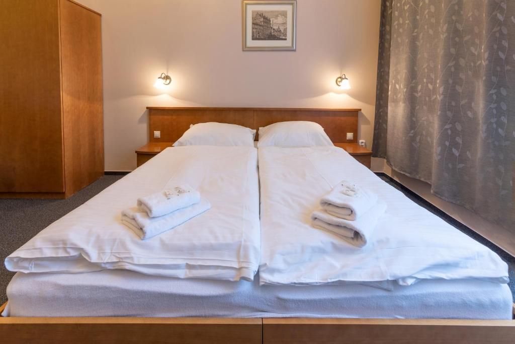 Een tweepersoonsbed met witte lakens en handdoeken, een houten hoofdbord en twee wandlampen.