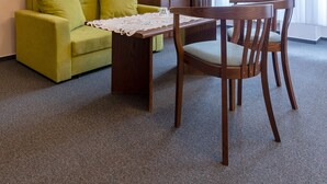 Ein Hotelzimmer mit einem grünen Sofa, einem Holzespeisetisch mit Stühlen, einem flachbildfernseher an der Wand und einem großen Fenster mit durchsichtigen Vorhängen.