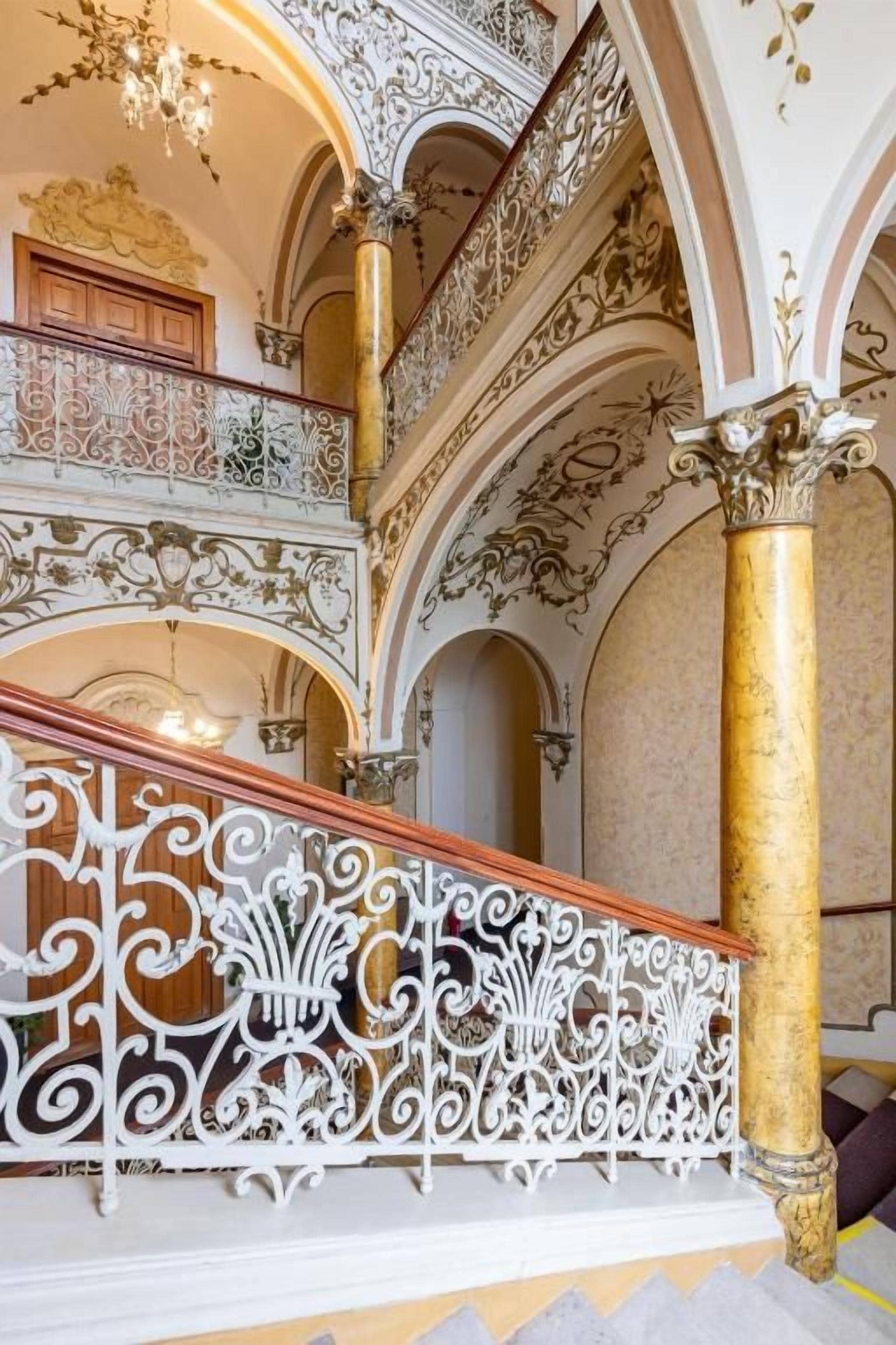 Una imponente escalera con barandales blancos ornamentados y un columnilla dorada.