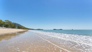A beach with clear blue water, sandy shore, and distant hills.