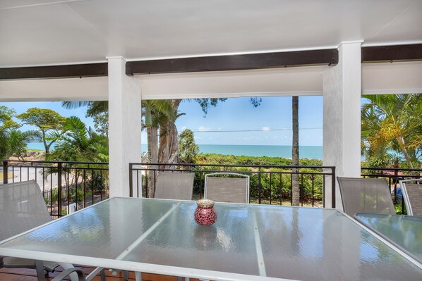 Relax in this ocean-view seating area with a glass table and metal chairs, surrounded by palm trees.