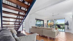Uma sala de estar espaçosa com escada moderna, um conjunto de sofás bege e grandes janelas com vista para o exterior.