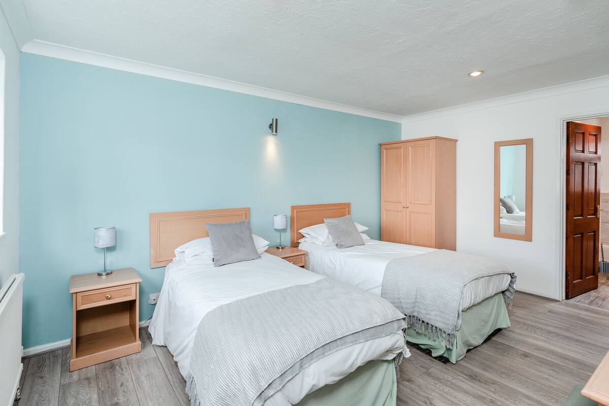 A bedroom with two beds, wooden nightstands, a wardrobe, and a mirror.