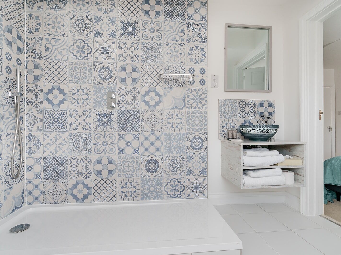 Une salle de bain avec une baignoire blanche, un lavabo avec un récipient bleu et un mur carrelé aux motifs bleus et blancs.