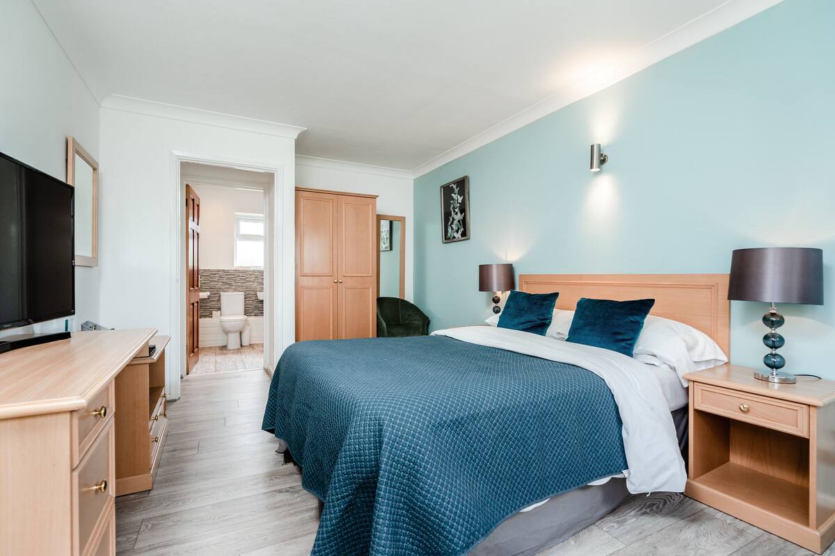 A bedroom with a bed, bedside tables, a TV, and a bathroom visible in the background.