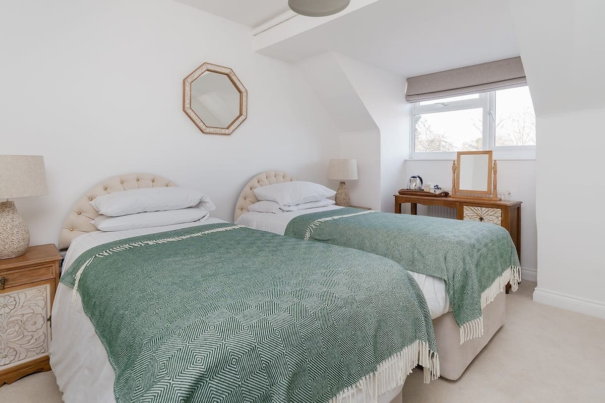 A bedroom with two beds, a window, and a mirror on the wall.