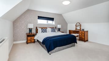 A bedroom with a sloped ceiling, a bed with a blue bedspread, two bedside tables with lamps, a dresser, and a window with a blue valance.