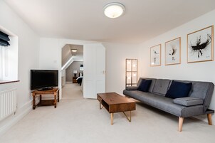 A modern living room with a grey sofa, wooden coffee table, and a flat-screen TV on a stand.