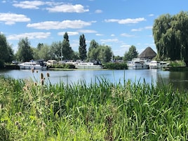 A calm river with boats docked along the shore, surrounded by lush greenery and trees.