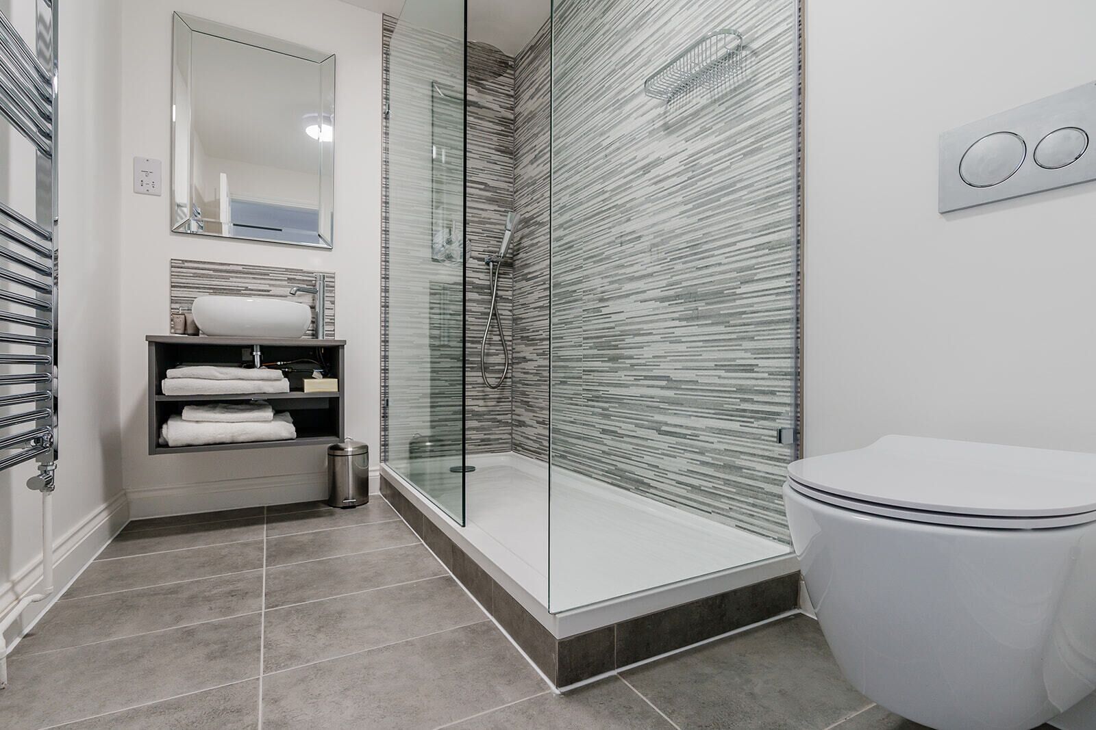 Un baño moderno con ducha de vidrio, inodoro blanco y lavamanos empotrado con espejo superior.