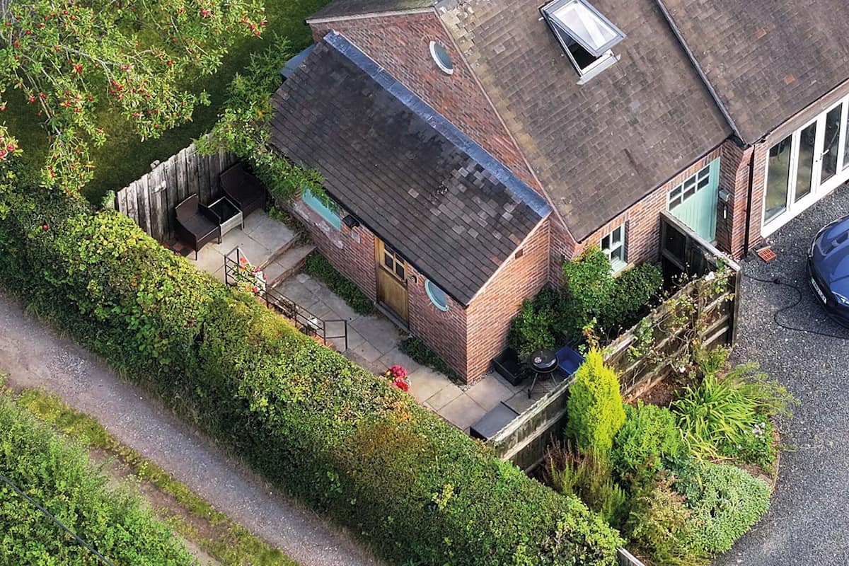 An aerial view of a house with a sloped roof, a visible chimney, and a small porch area with outdoor seating.