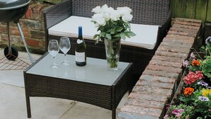 A wicker table with a bottle of wine and glasses, set against a wooden fence. - Pine Tree Lodge Bridgnorth (Bridgnorth)