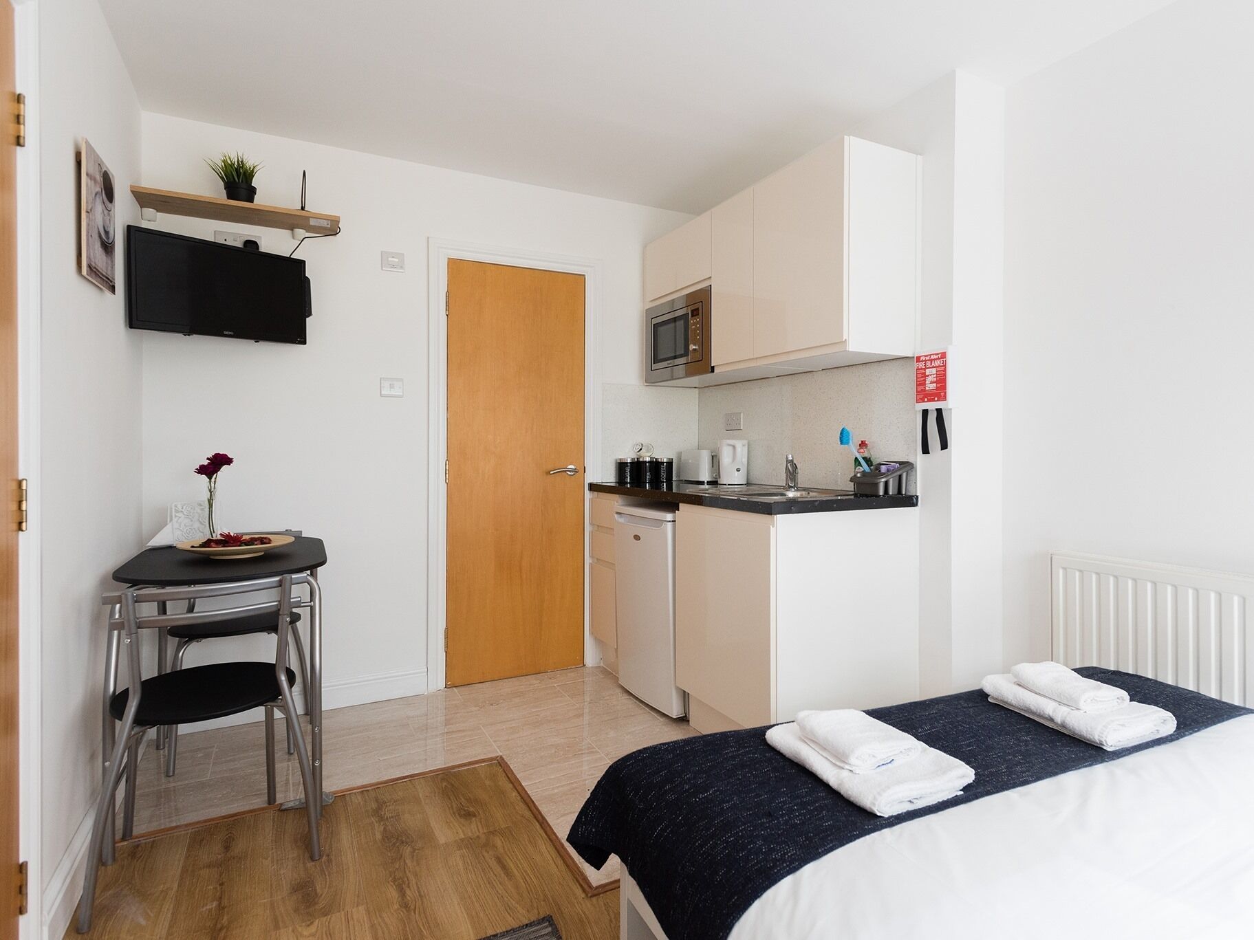 A compact room with a bed, a small kitchenette, a dining area, and a door.