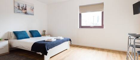A bedroom with a bed, bedside table, lamp, and a window with a view of buildings.