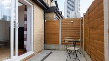 A small patio area with a wooden fence, a sliding glass door, and a table with chairs.