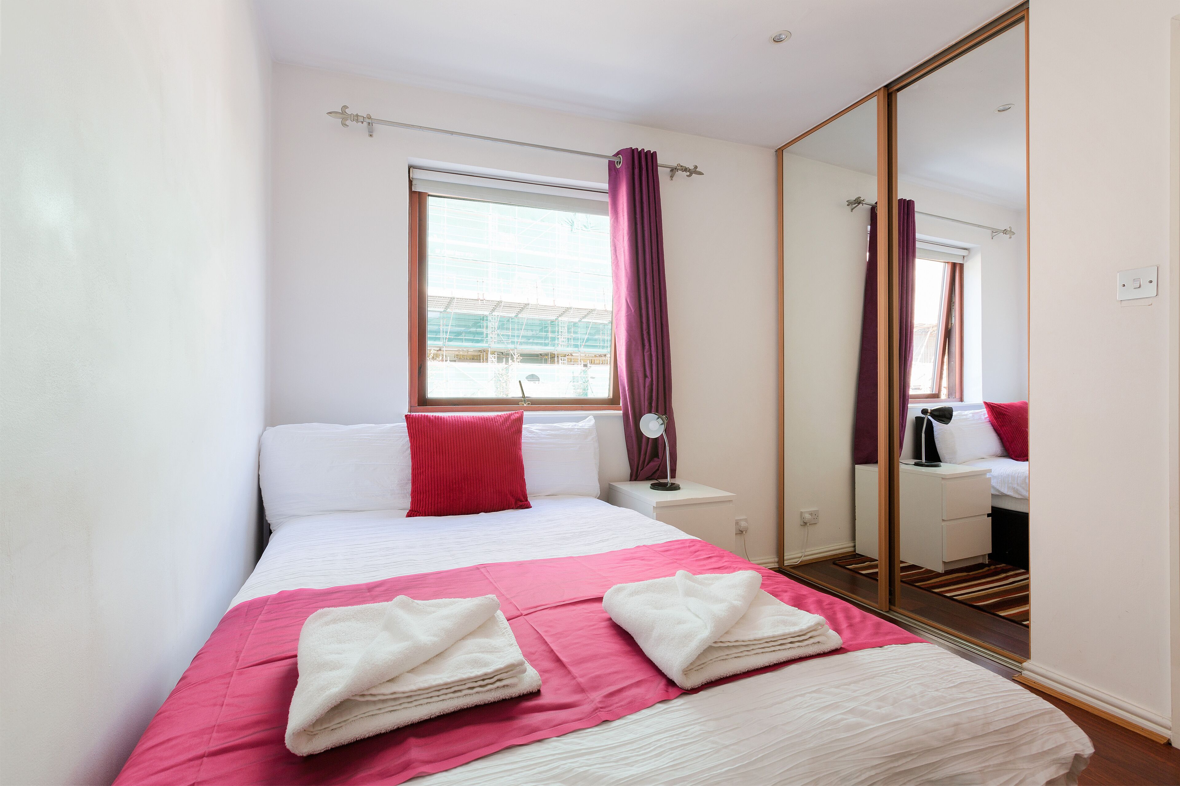 Une chambre d’hôtel avec un lit, une table de chevet, un miroir et une fenêtre avec des rideaux.