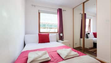 A hotel room with a bed, a nightstand, a mirror, and a window with curtains.