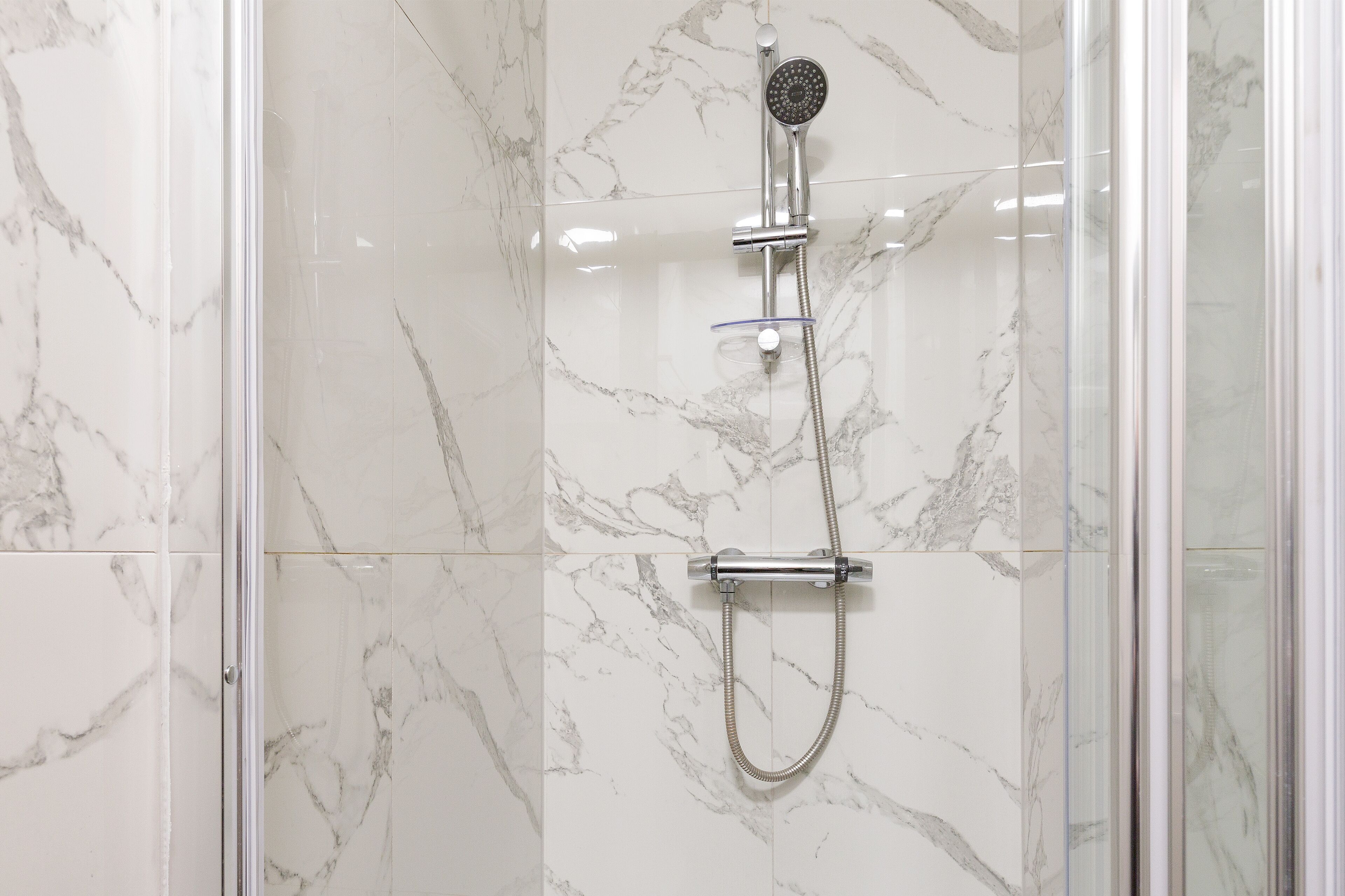 A shower with a handheld showerhead and a handheld hose, set against a marble wall.