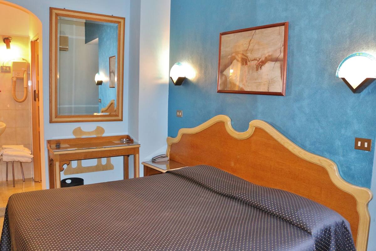 A bedroom with a wooden bed, a nightstand, a mirror, and a wall-mounted light fixture.