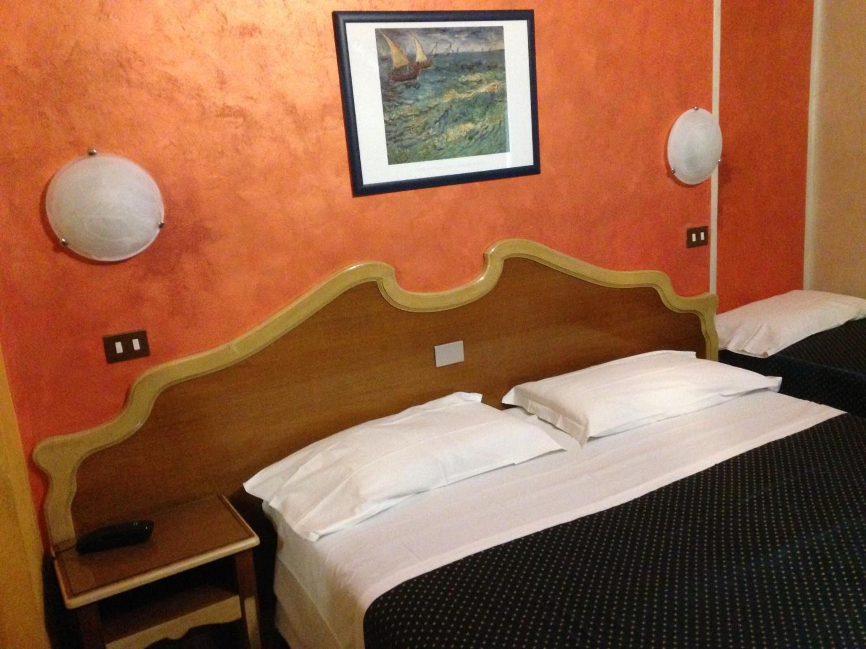 Ein Hotelzimmer mit einem Einzelbett, einem Nachttisch, einem gerahmten Bild eines Segelbootes an der Wand und zwei Wandlampen.