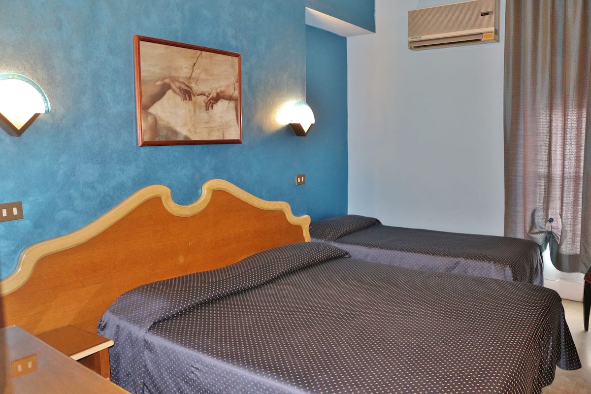 A room with two beds, a wooden headboard, a wall-mounted picture, and a ceiling air conditioner.