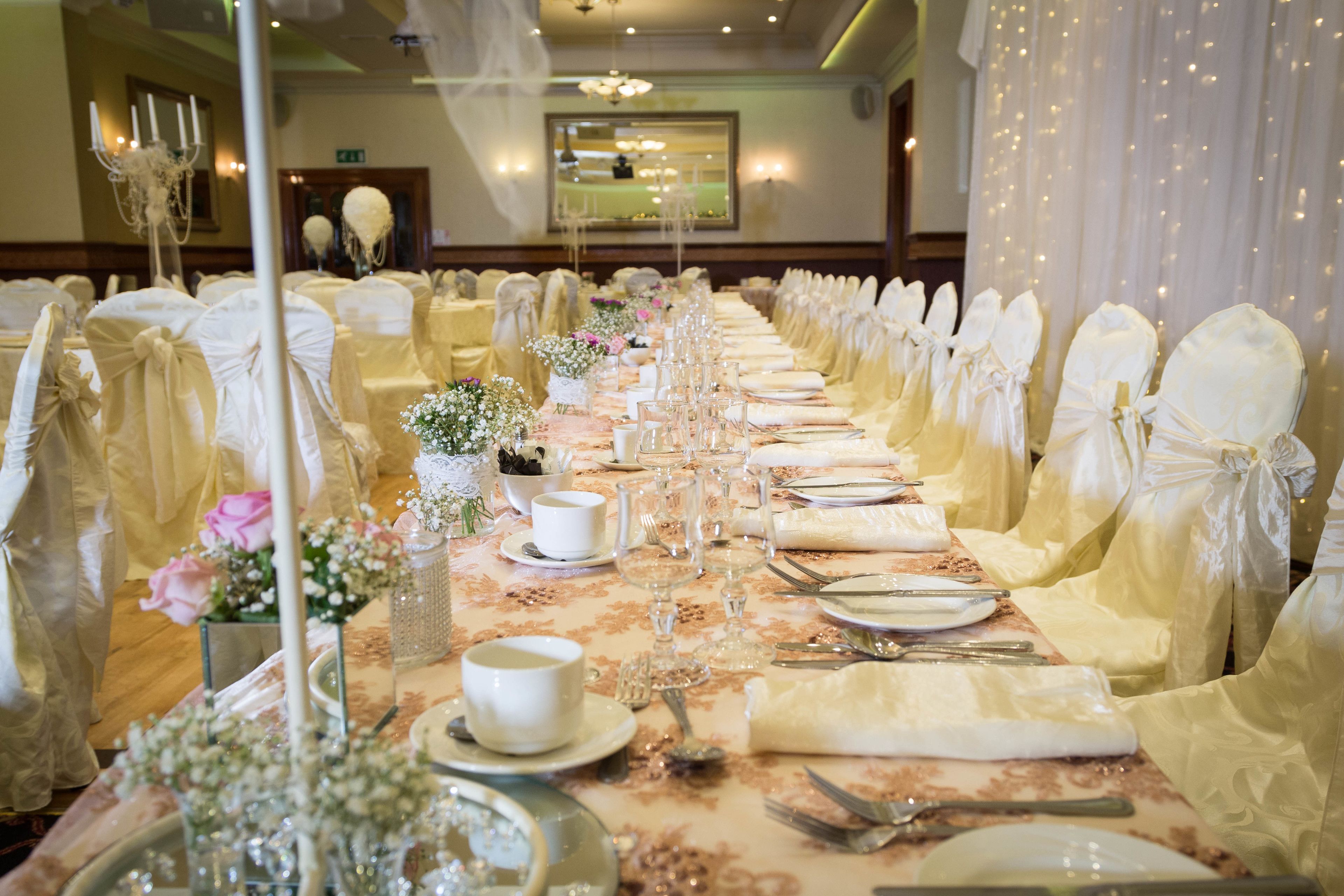 Una mesa de banquete dispuesta para un evento formal, con manteles blancos, cristalería y centros de mesa florales.