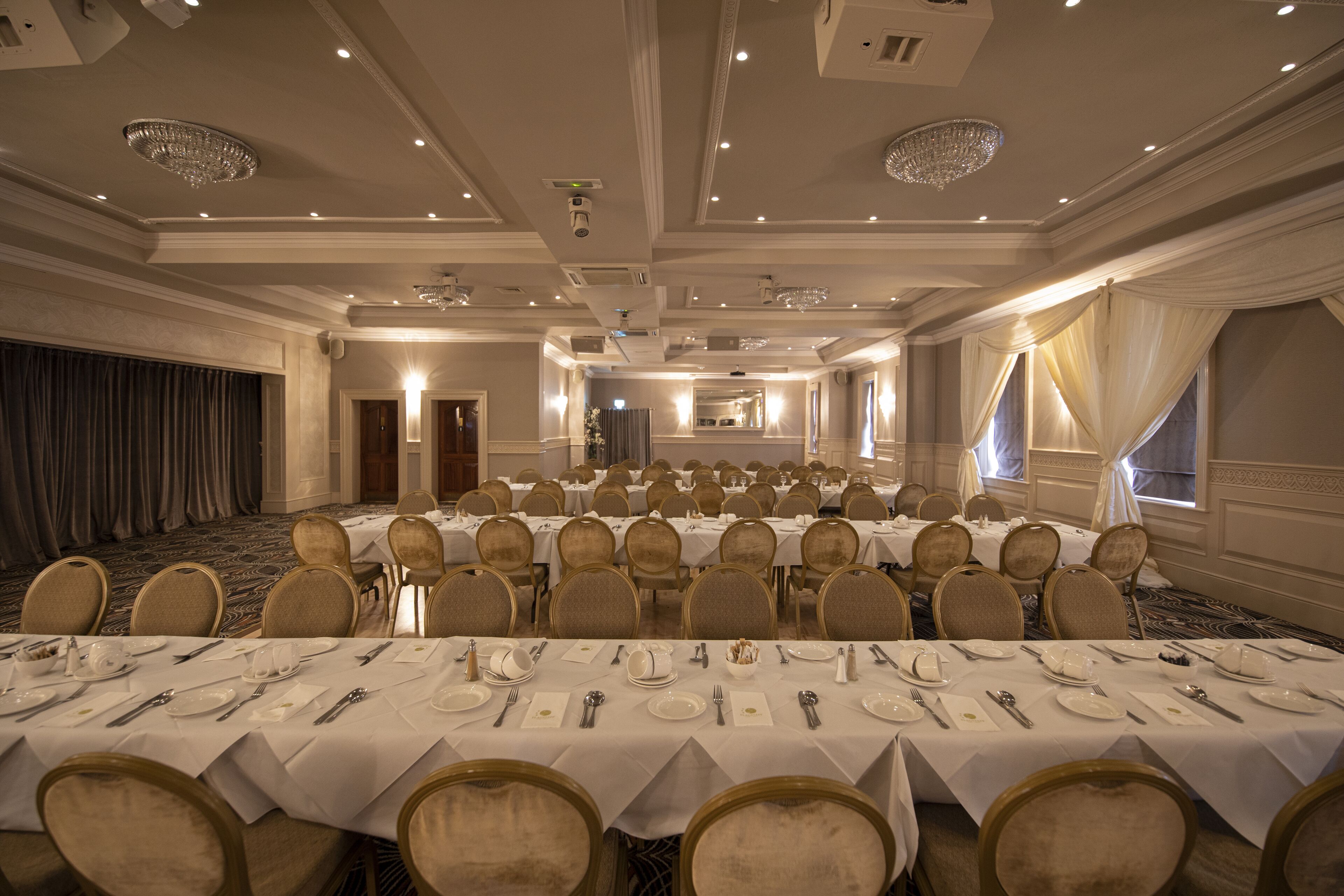 A banquet hall with multiple round tables set for dining, equipped with white tablecloths, chairs, and dining utensils.