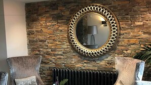 Una habitación con pared de piedra, un espejo redondo, dos sillones, una mesita de centro y un radiador.