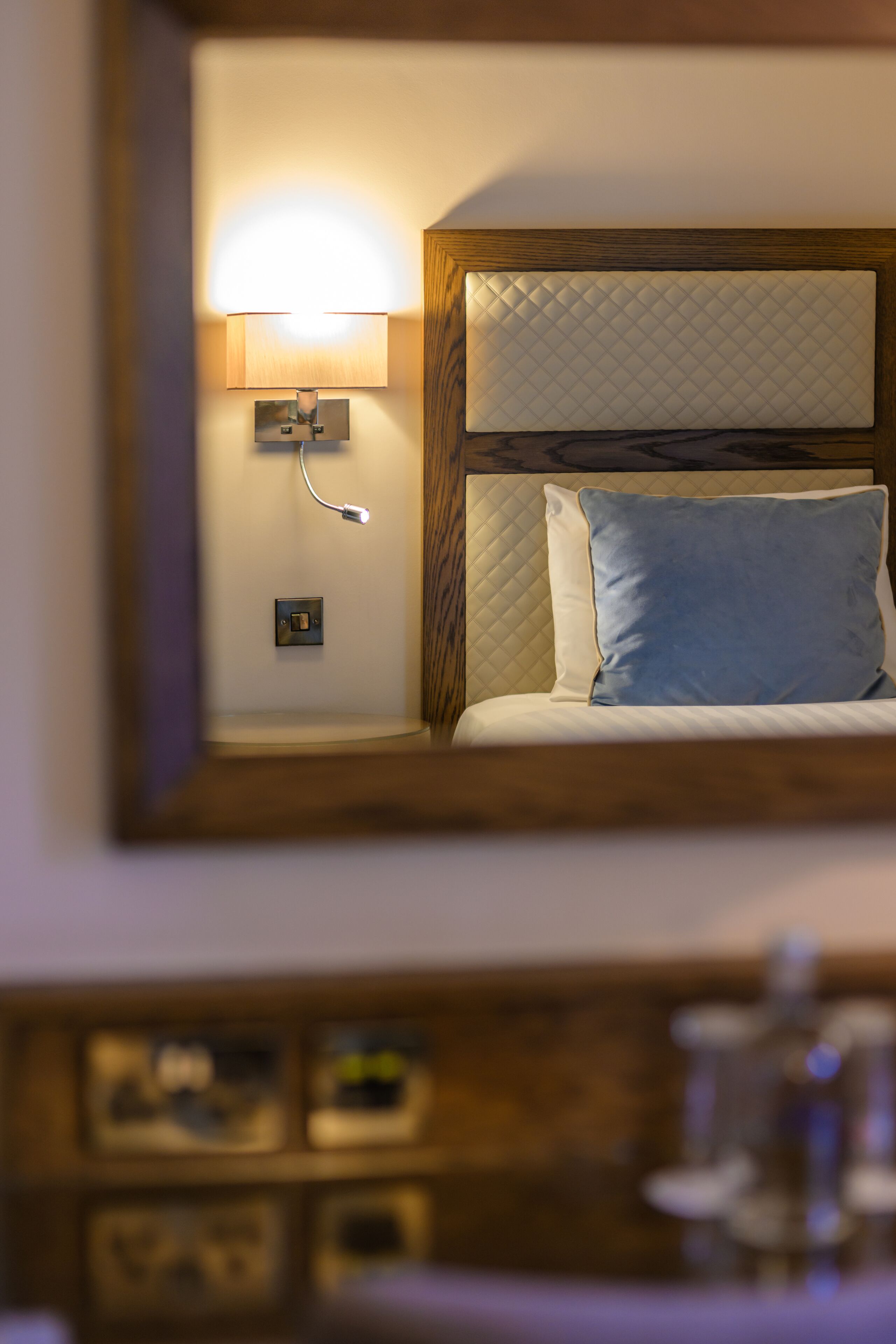 Une chambre d’hôtel avec un lit, une table de chevet, une lampe et un miroir qui reflète la pièce.