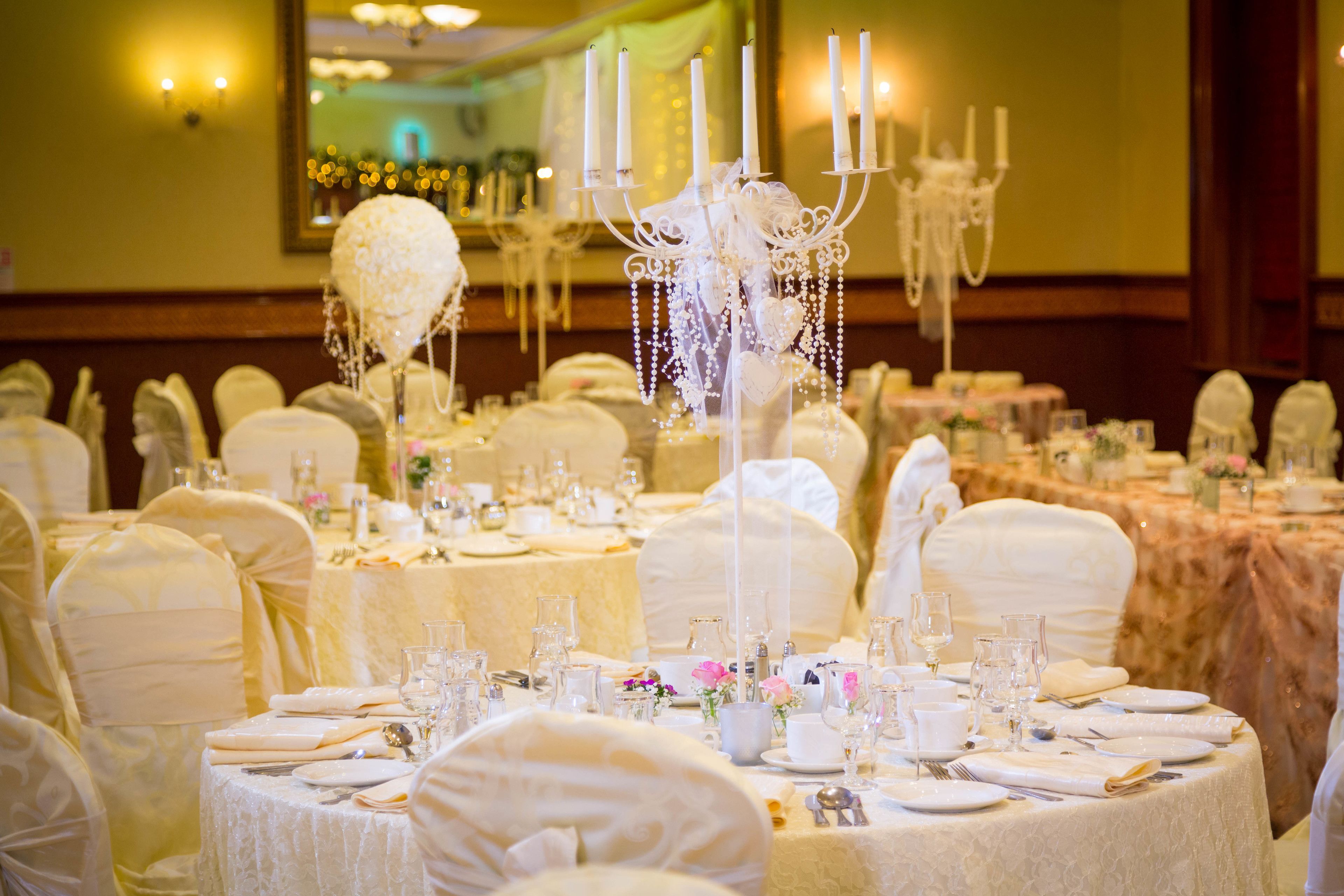 Un salón de banquetes con mesas redondas dispuestas para un evento formal, con manteles blancos, cristalería y centros de mesa florales.