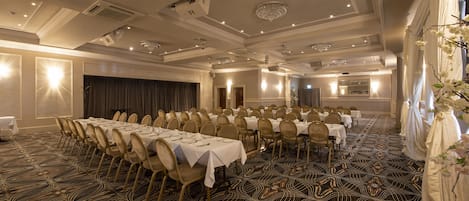 A banquet hall with long tables set for dining, arranged in rows, and a patterned carpet.