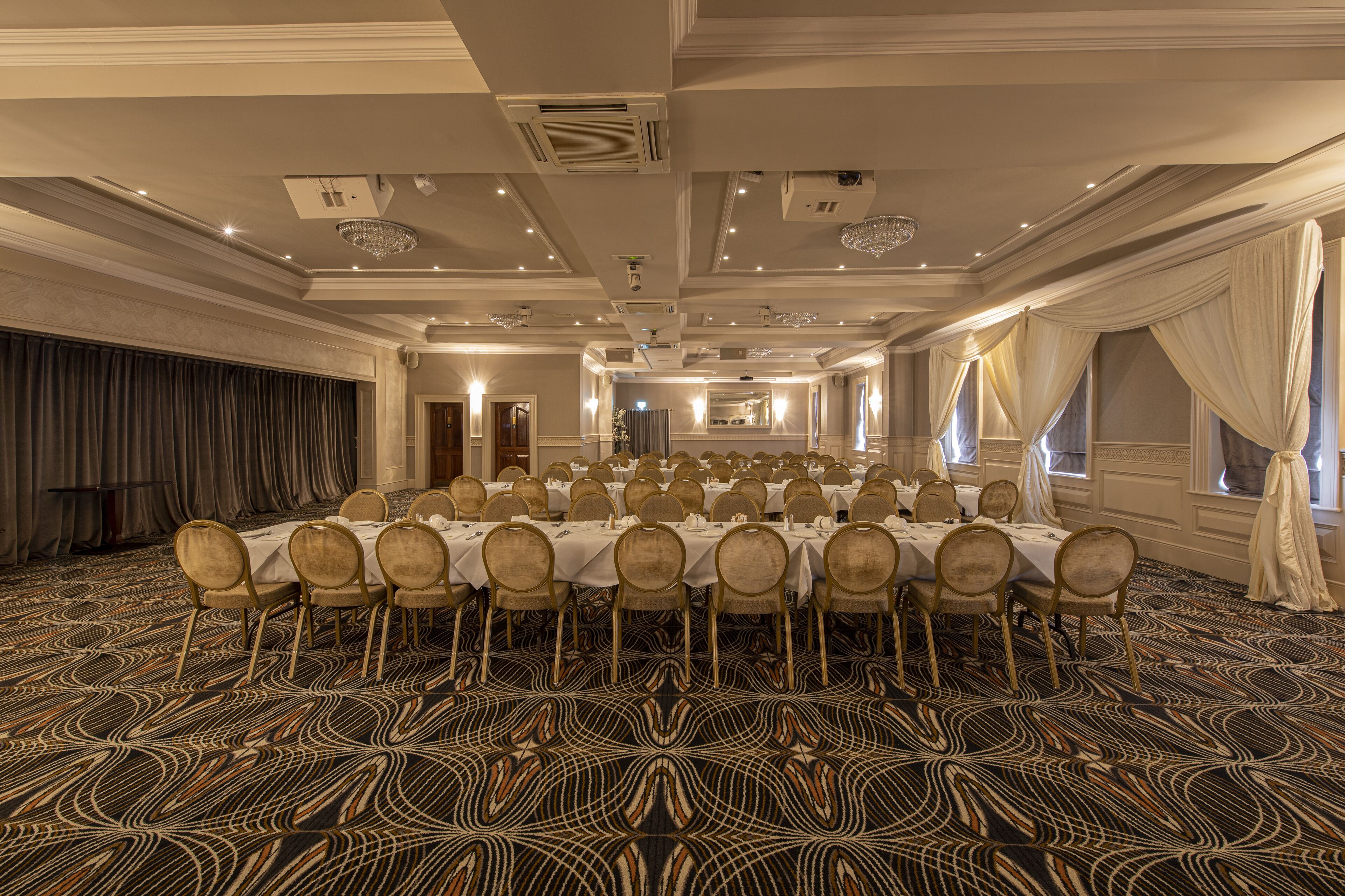 A banquet hall with round tables and chairs, a patterned carpet, and a chandelier.