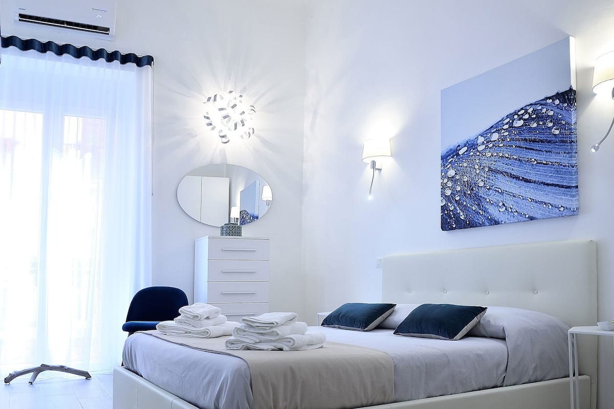 Een moderne slaapkamer met een bed, een dressoir, een spiegel en een kunstwerk aan de muur.