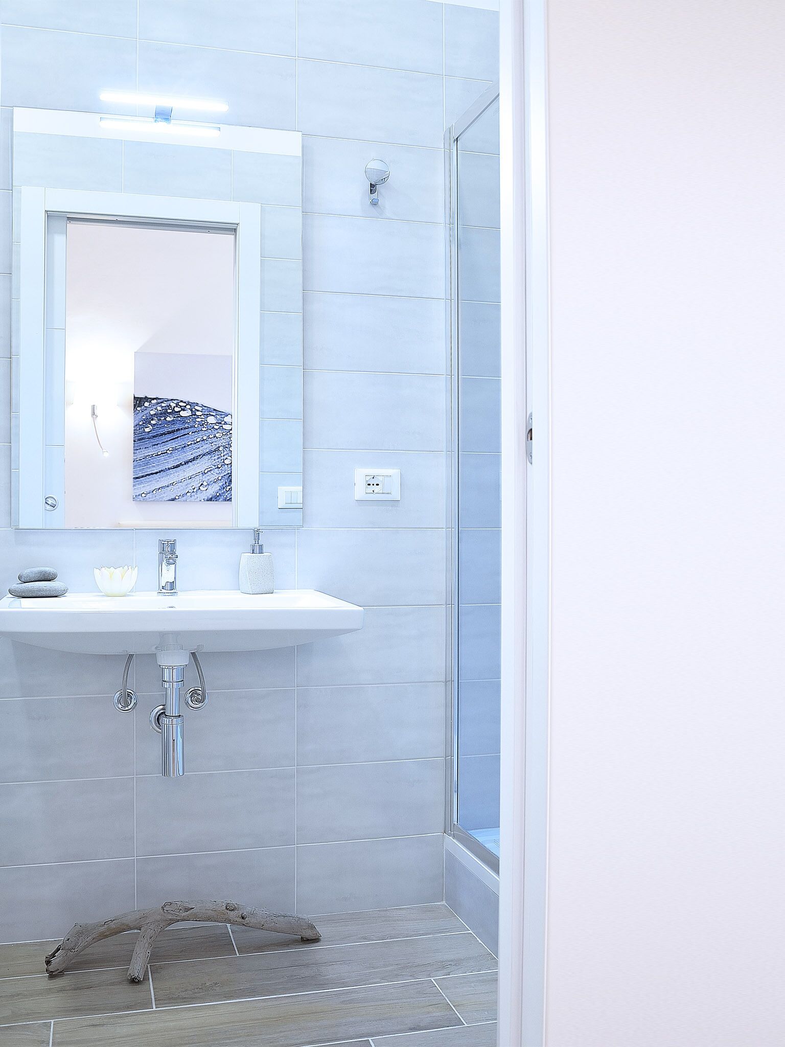 A modern bathroom with a white sink, a mirror, and a shower area.