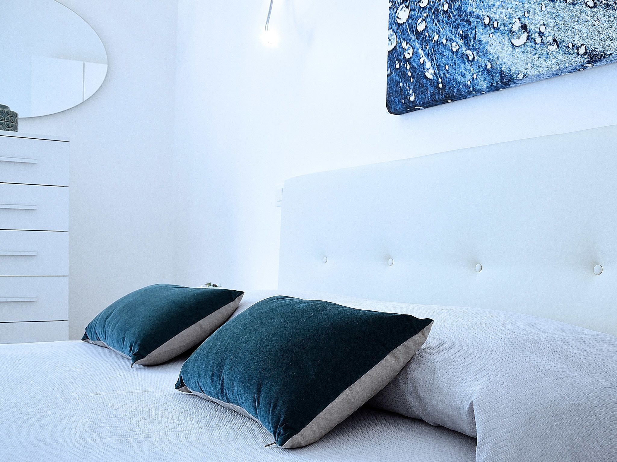 A bedroom with a bed, two pillows, a dresser, a mirror, and a wall art piece.