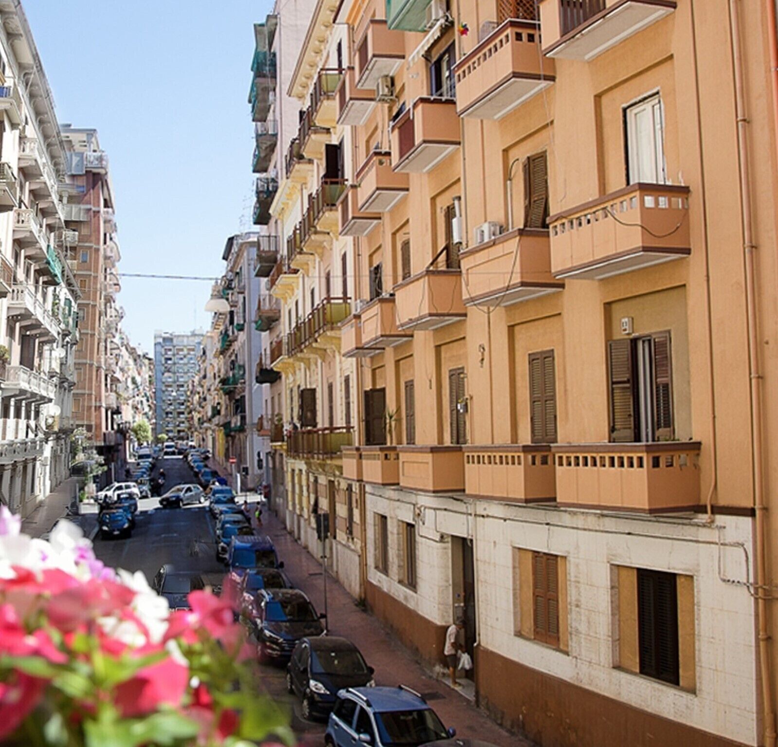 A narrow street lined with multi-story buildings, featuring balconies and a clear sky.