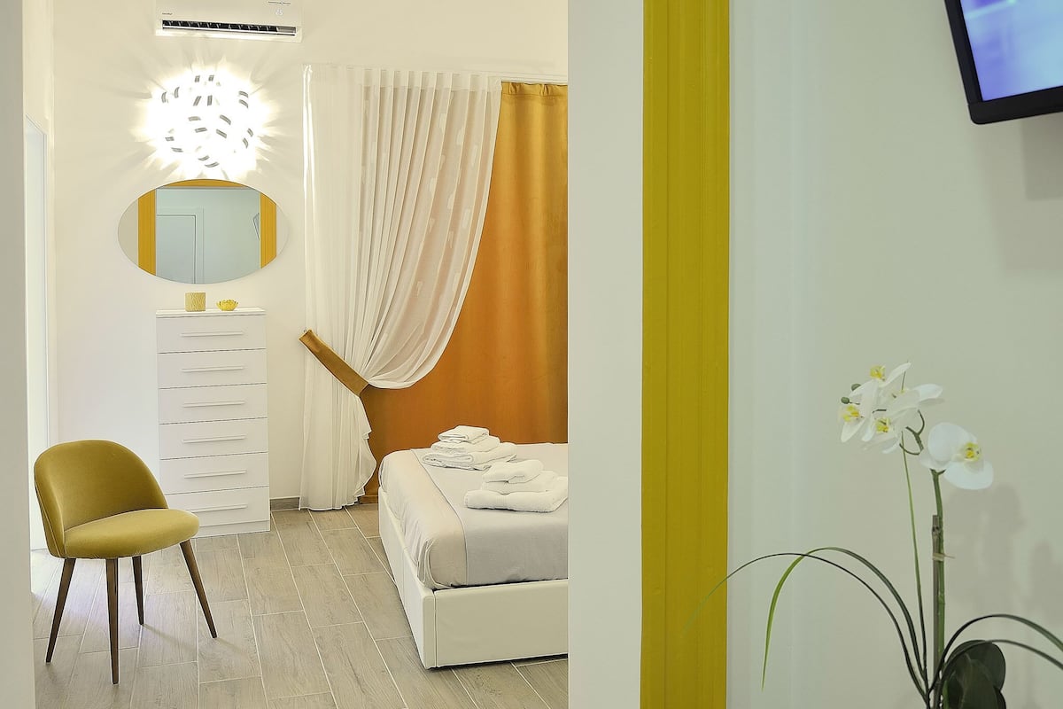 Een hotelkamer met een bed, een stoel, een kaptafel met spiegel en een potorkidee.