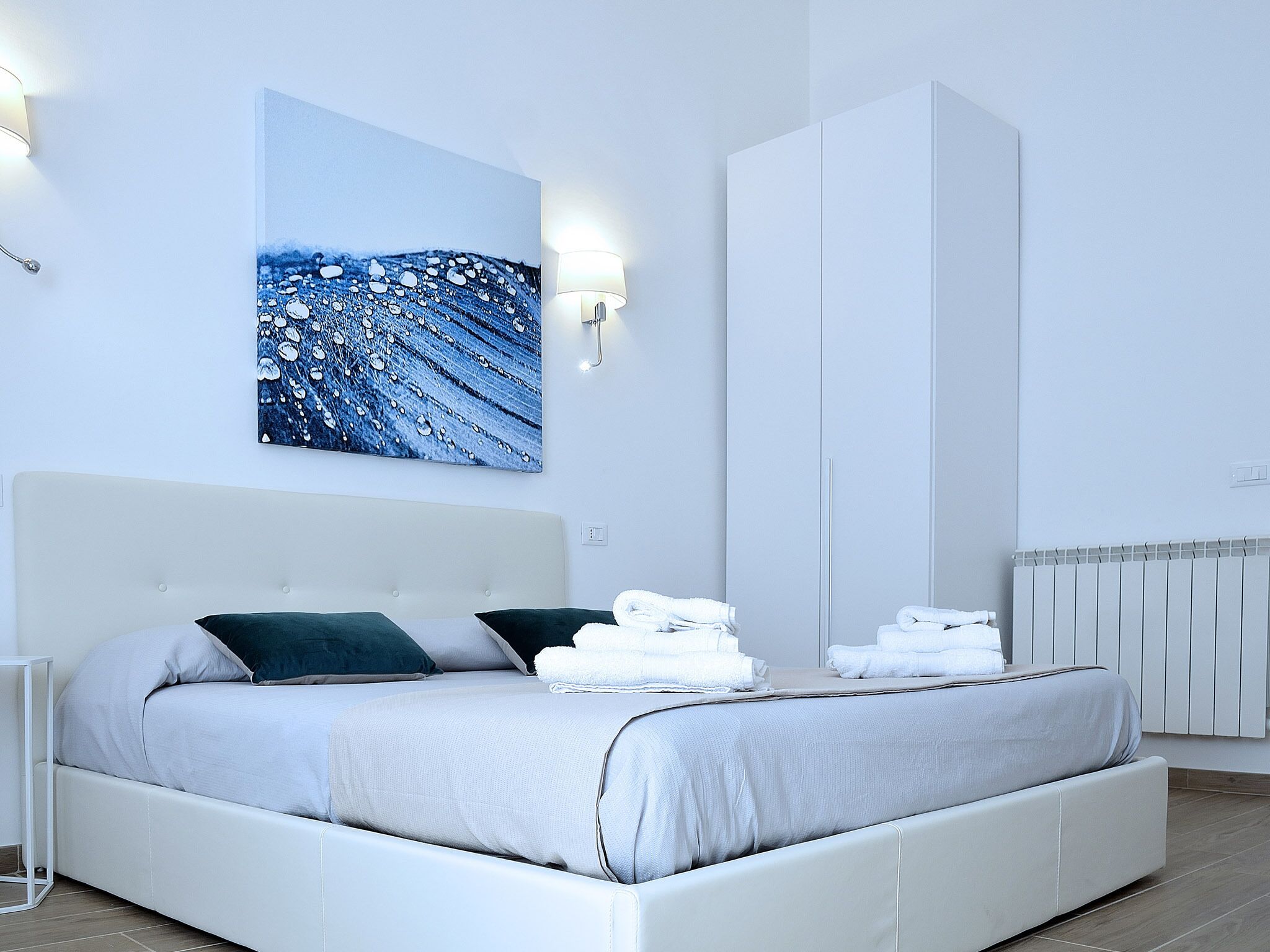 A modern bedroom with a large bed, a wardrobe, and a wall-mounted artwork.