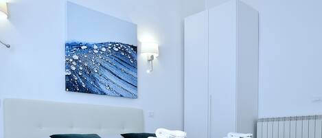 A modern bedroom with a large bed, a wardrobe, and a wall-mounted artwork.