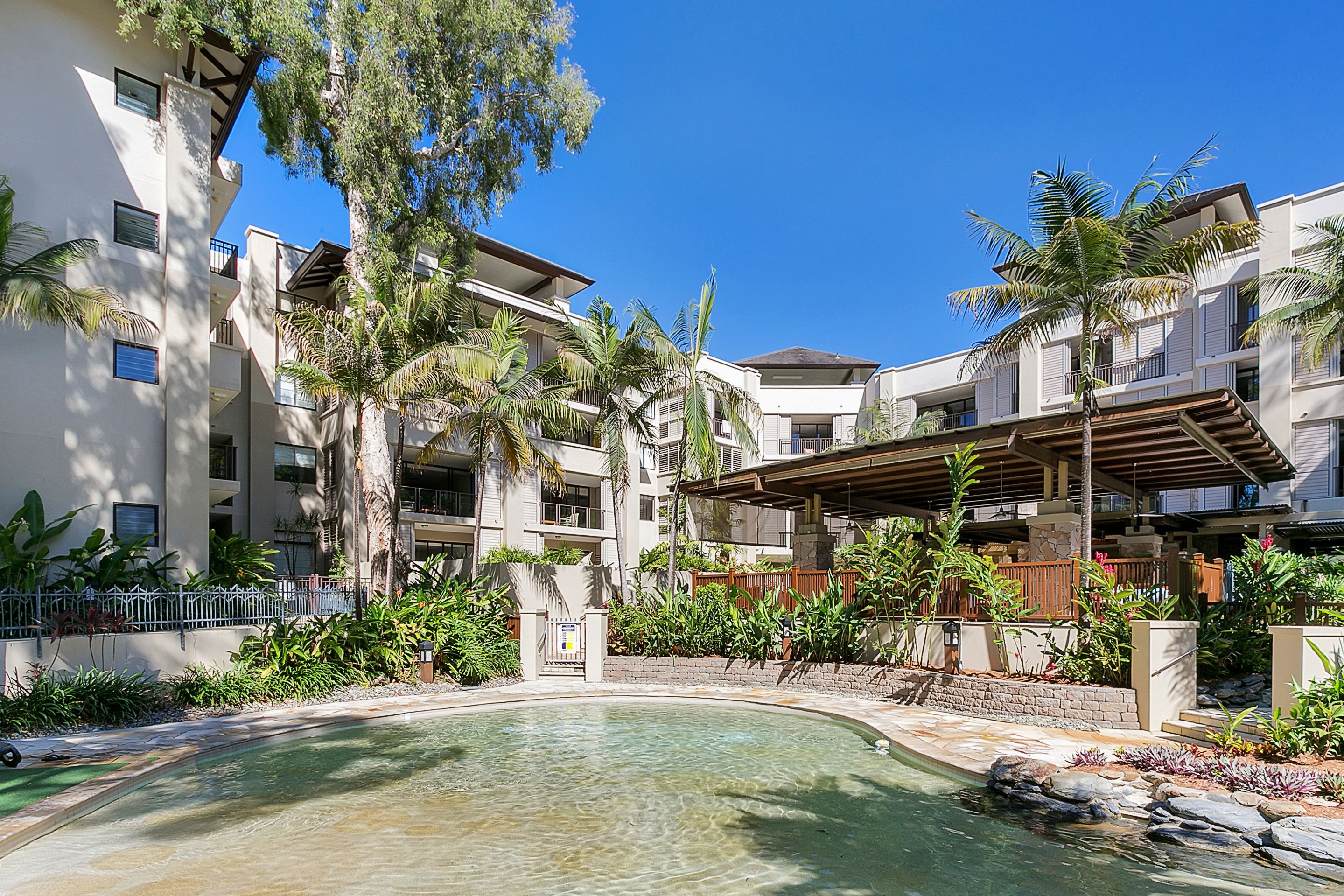 Un resort con piscina rodeada de palmeras y un patio cubierto.