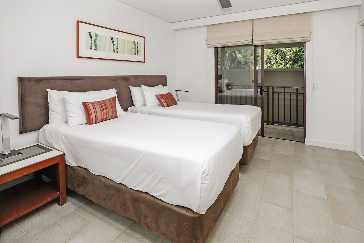 A hotel room with two beds, a nightstand, a framed picture on the wall, and a balcony with a view.