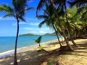 A beach with palm trees, clear blue water, and a distant island.