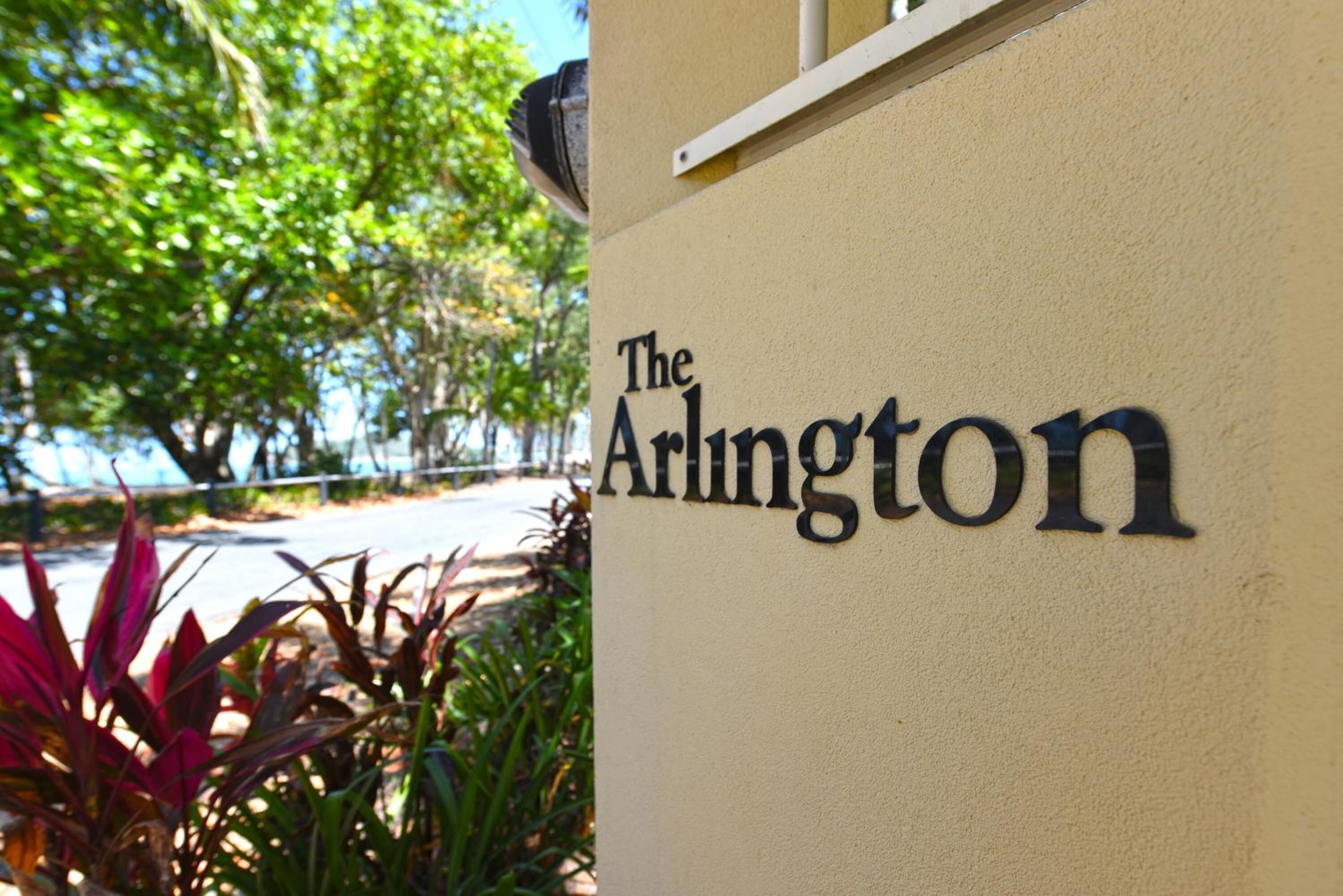 Beigen värinen seinä, jossa on kyltti, jossa lukee ”The Arlington”, ja sen ympärillä on vihreää kasvillisuutta.