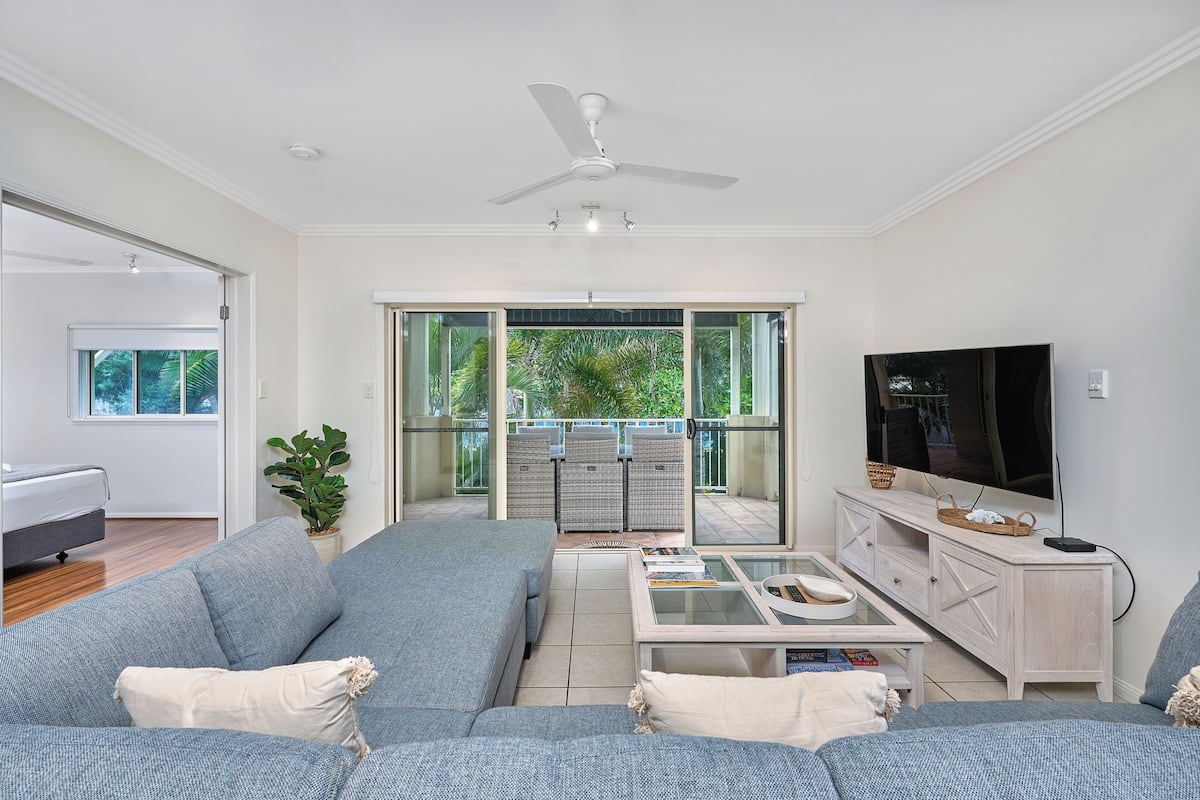 A living room with a sofa, coffee table, TV, and a balcony with outdoor furniture.